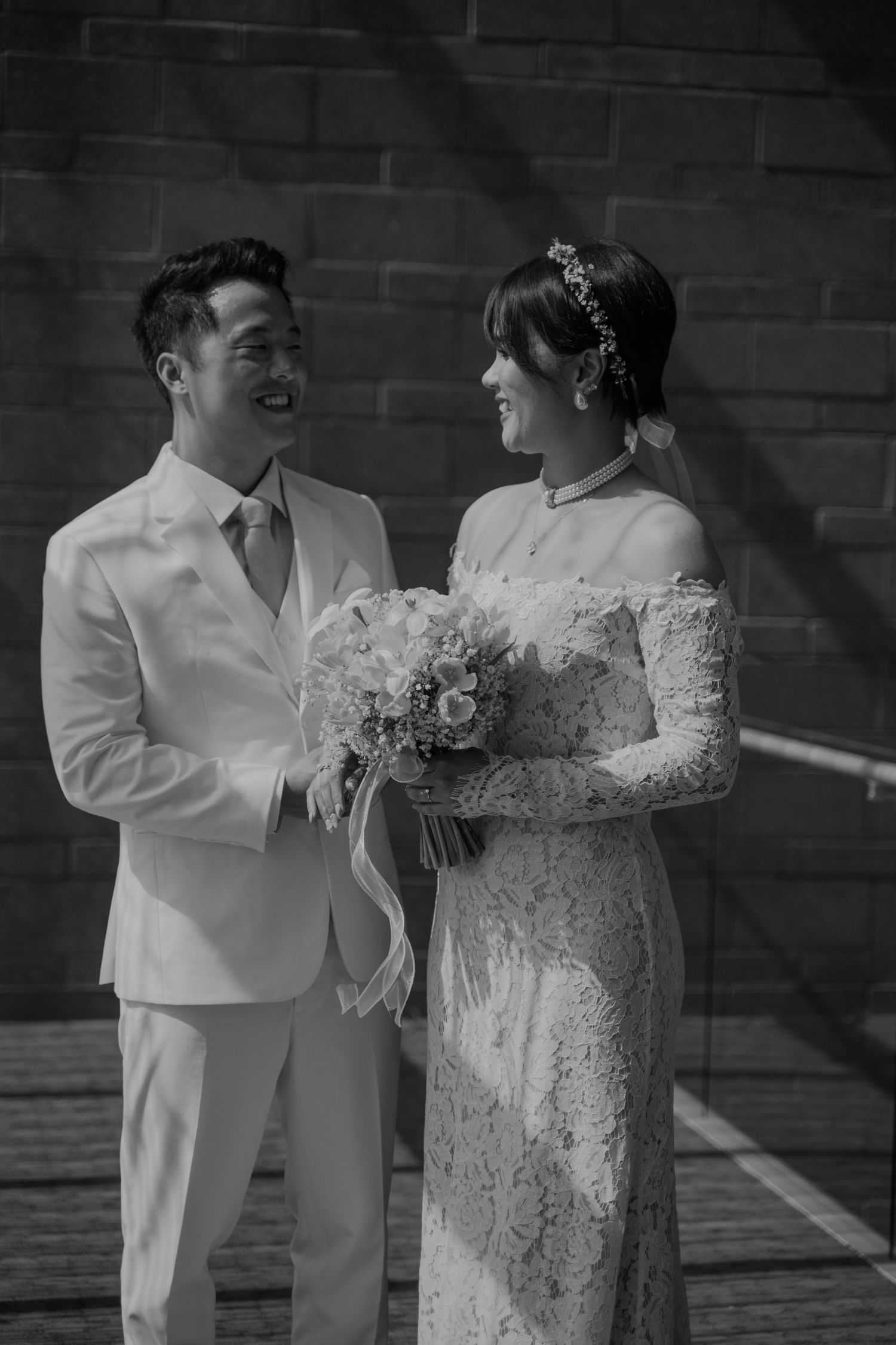 A black and white wedding photo showing a couple in elegant attire with the bride holding a delicate floral bouquet.