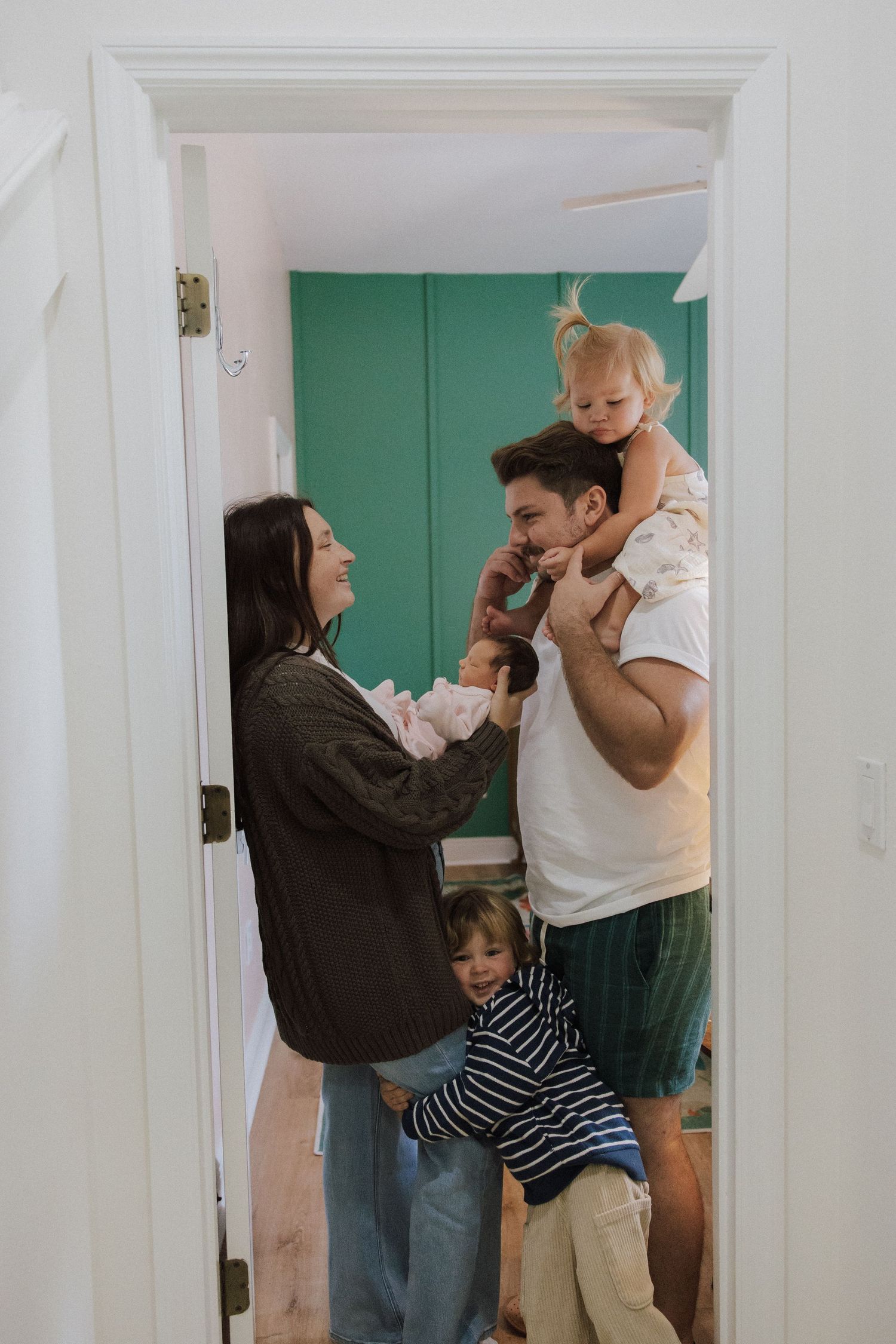 A sweet family moment captured in black and white as they playfully interact near a doorway with mint green walls.