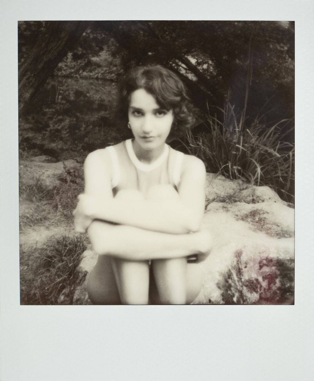 Black and white vintage Polaroid photograph showing person in natural outdoor setting seated on a rock.