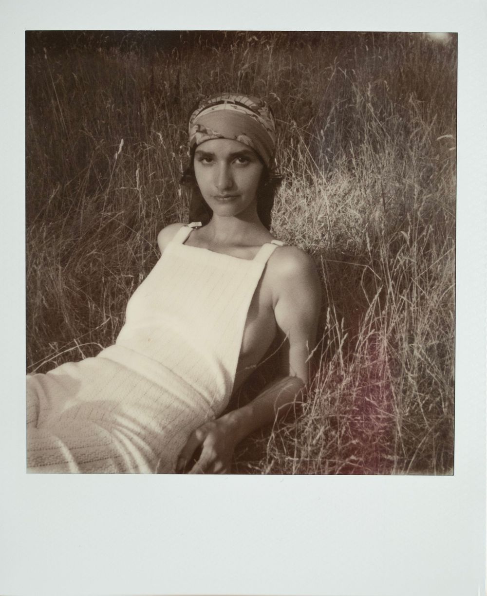 Vintage Polaroid photograph showing a person wearing a white sleeveless top and headpiece in tall grass.