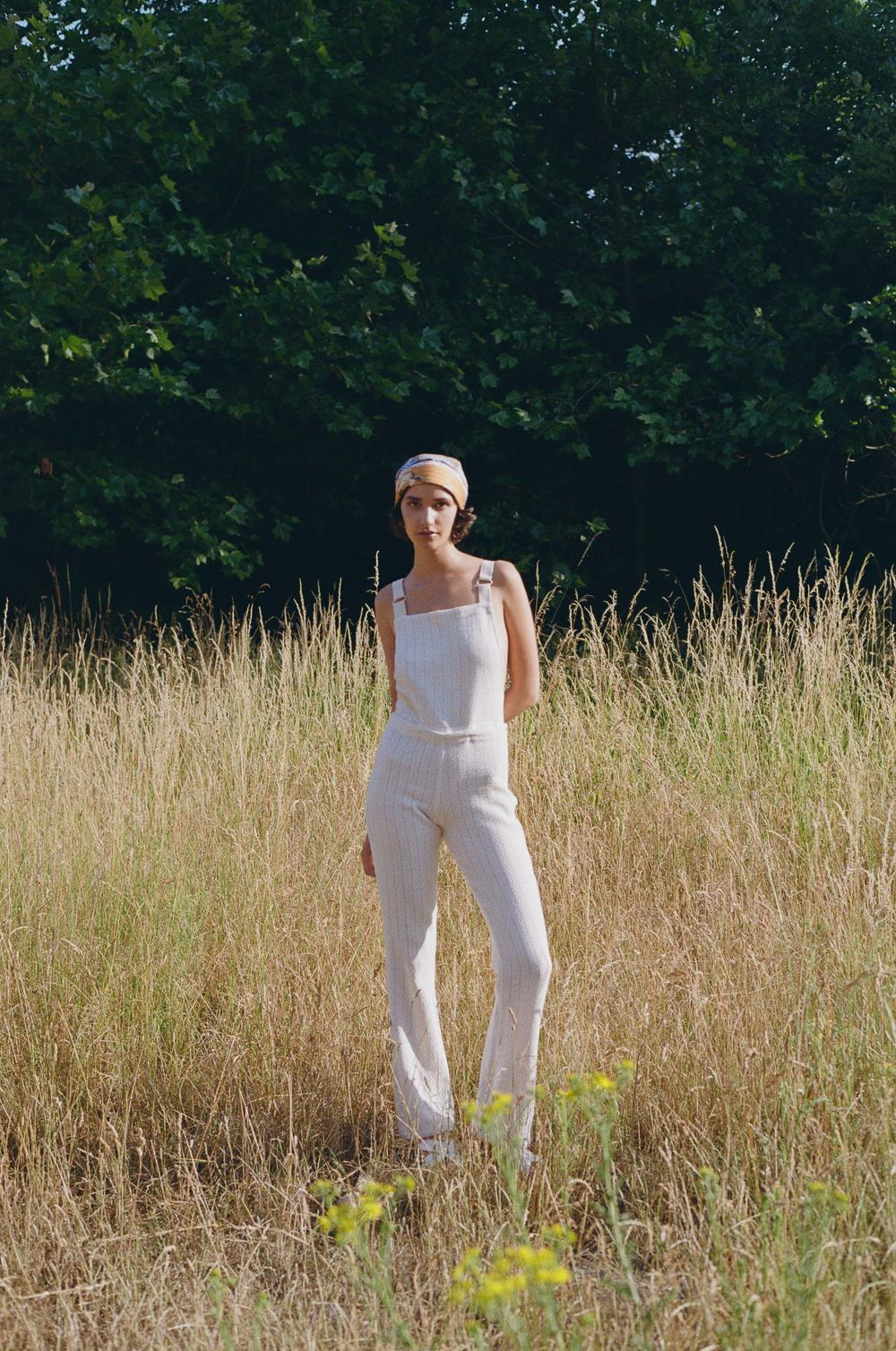 Person wearing all white walks through a sun-lit field of tall golden grass on a summer day.