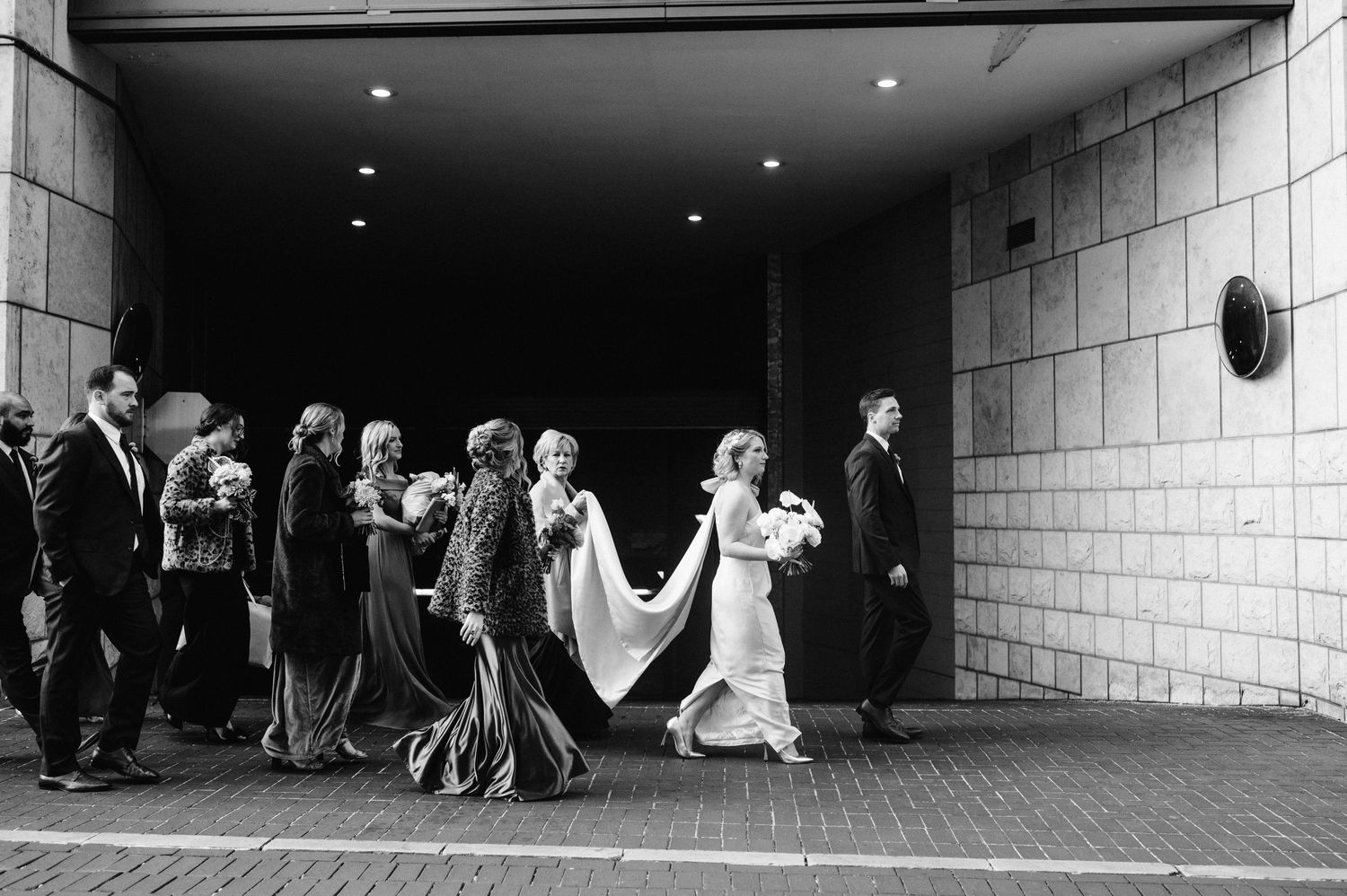 Wedding party walking through dark tunnel with couple leading the procession.