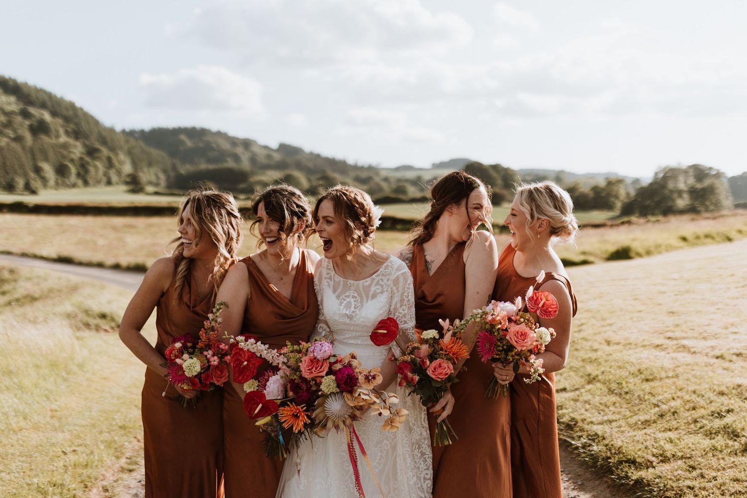 Wedding party stands together against scenic mountain backdrop in coordinating burgundy and rust colored attire.