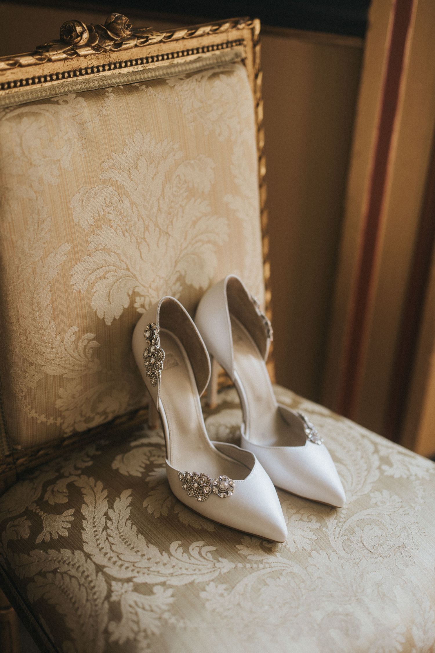 Elegant white bridal heels resting on an ornate lace textured surface in warm lighting - taken by Grimsby photographer.
