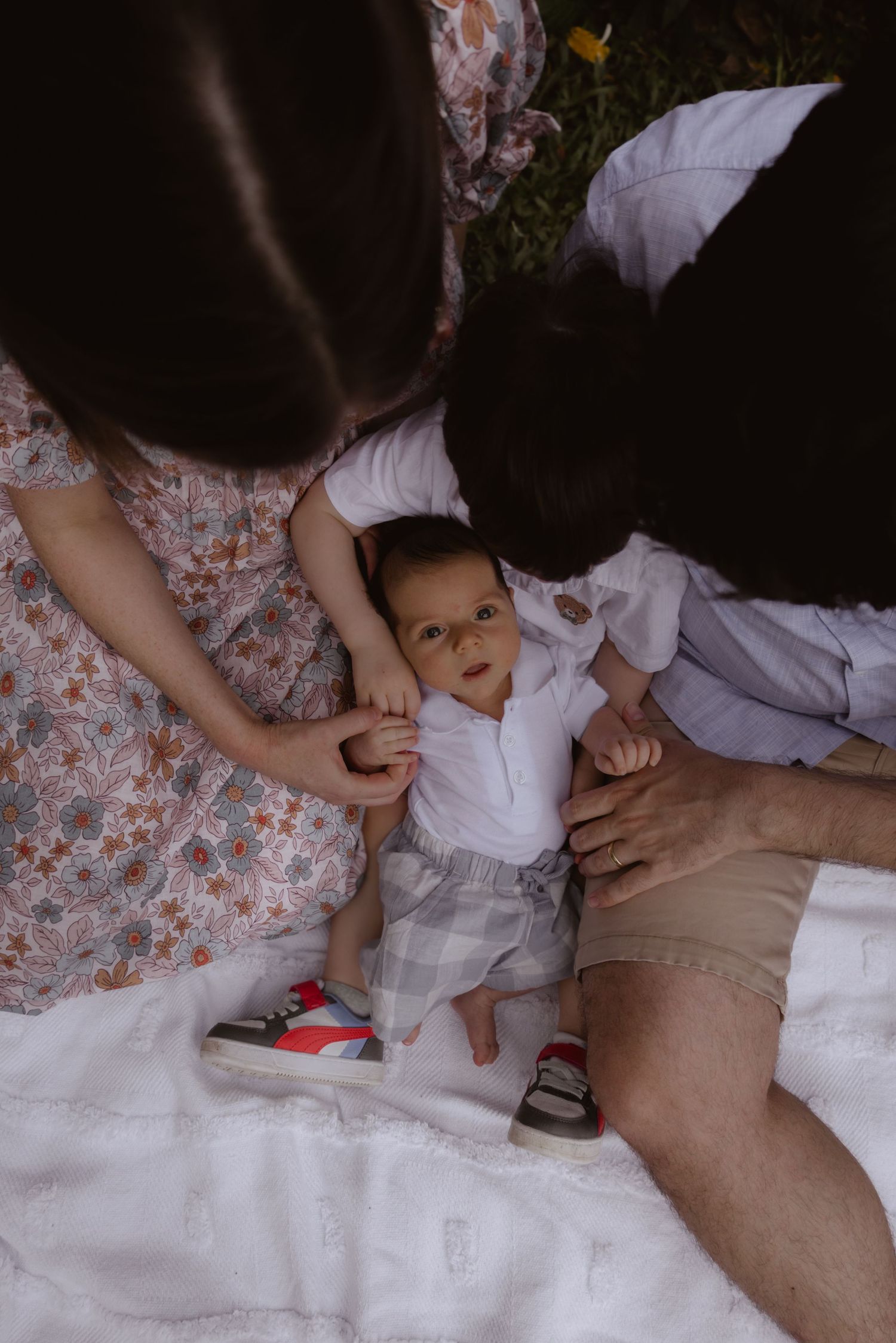 Intimate family moment captured on a white blanket in a garden setting.