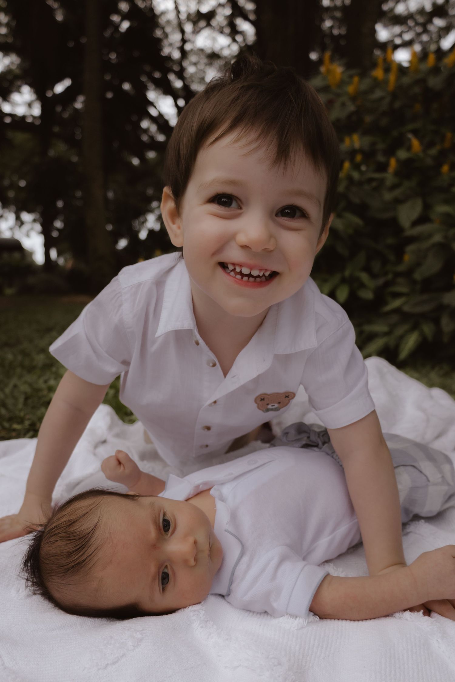 Siblings sharing playful moments together on a white blanket outdoors.