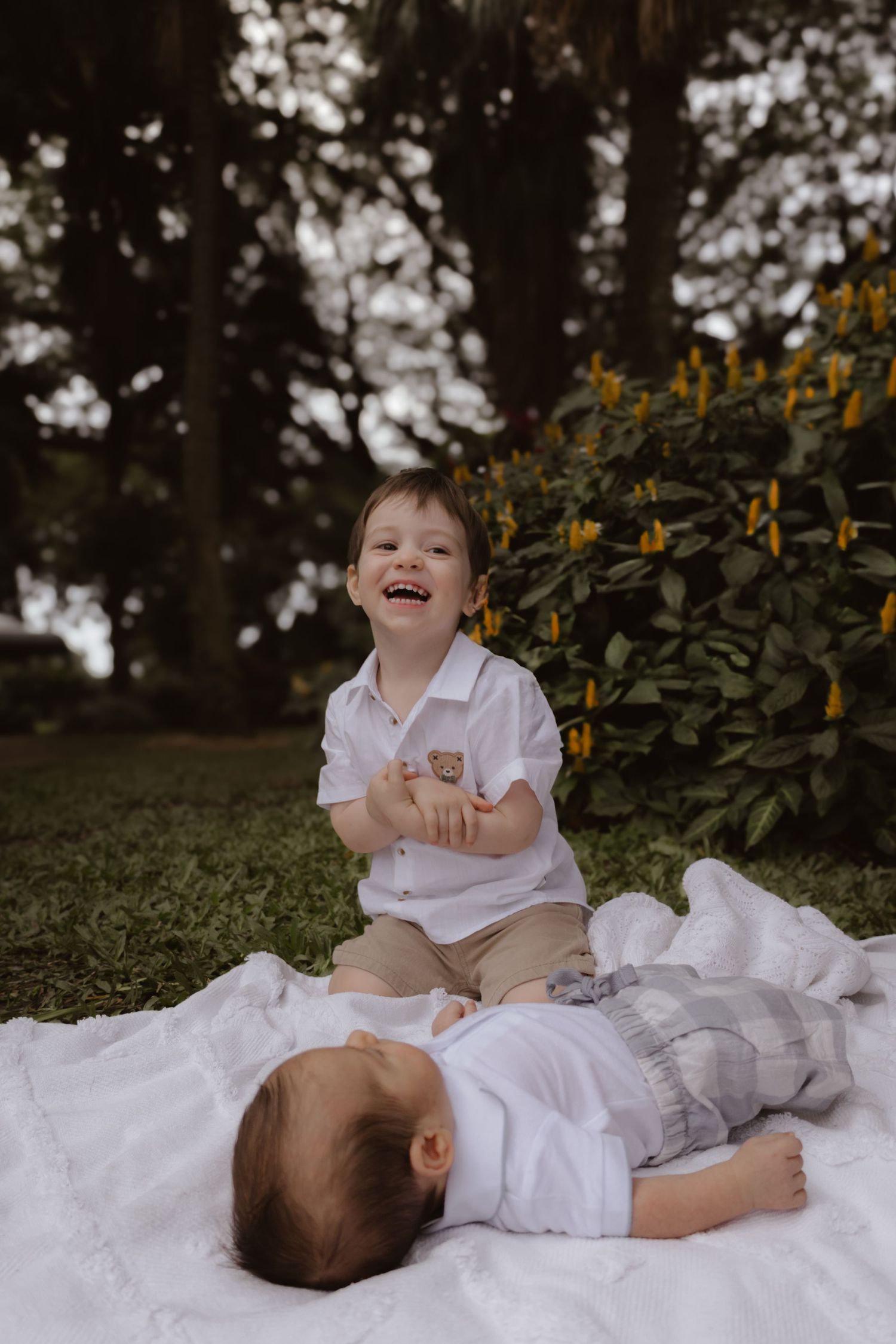 Children playing and laughing together on a white blanket outdoors with flowers in background.
