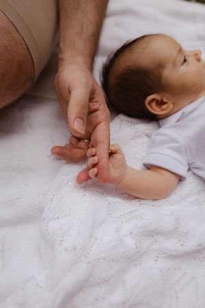Gentle hand holding baby's tiny fingers on white lace blanket.