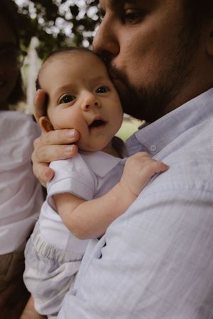 Close-up tender moment between parent and baby against natural backdrop.