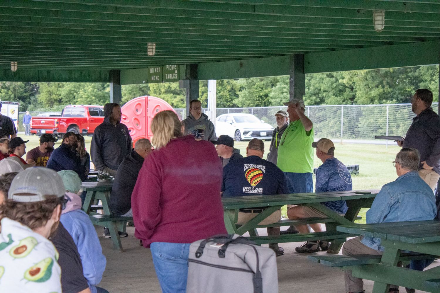 Crowd gathered under green pavilion shelter at outdoor event.