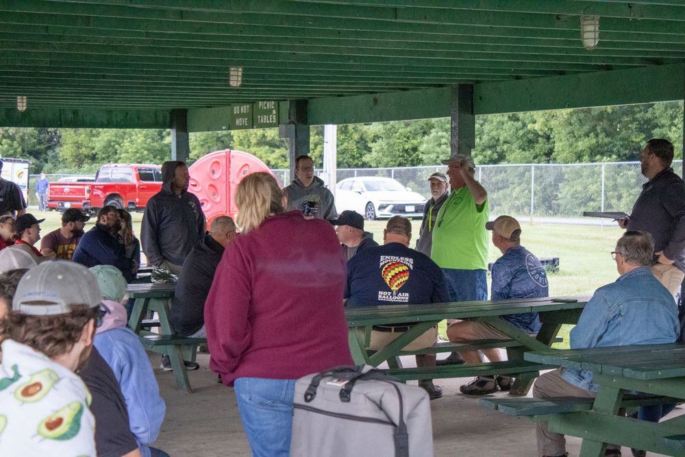 Crowd gathered under green pavilion shelter at outdoor event.