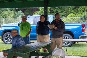 People sitting at picnic tables under green shelter during outdoor gathering.