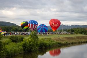 Hot air balloons preparing for launch near water with crowd gathered on shore.