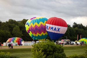 Colorful hot air balloons inflating on grassy field with spectators watching.