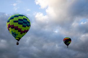 Green and yellow checkered hot air balloon ascending into cloudy skies during a festival.