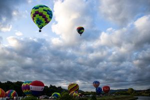 Hot air balloons take flight against dramatic cloud formations during an evening launch.