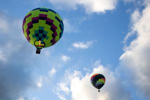 Colorful hot air balloon with geometric patterns floating in a bright blue sky with white clouds.
