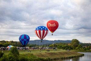 Hot air balloons with patriotic designs hovering over a serene waterway.