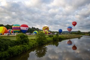 Collection of colorful hot air balloons reflected in calm waters during a balloon festival.