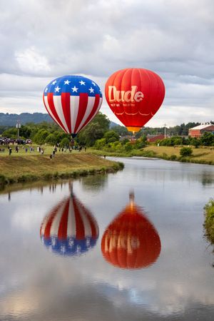 Stars and stripes hot air balloons creating perfect reflections in still water below.