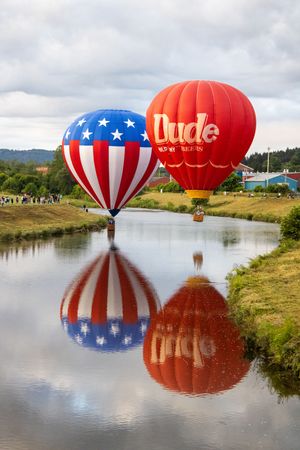 American-themed hot air balloons hovering low over a tranquil lake creating mirror reflections.