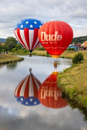Red, white and blue hot air balloons reflecting in a calm lake during a balloon festival.