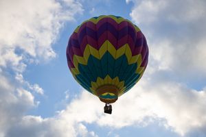 Geometric patterned hot air balloon silhouetted against bright clouds in blue sky.