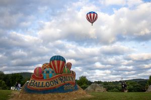 Hot air balloons floating over a grassy hill with cloudy skies in the background.