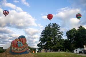 Multiple hot air balloons taking flight over a grassy field during a balloon festival.