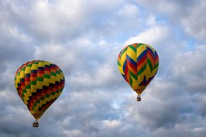 Colorful geometric patterned hot air balloons floating against a cloudy blue sky.