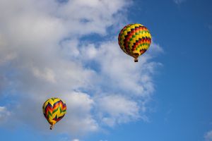Colorful checkered and geometric patterned hot air balloons floating through puffy clouds.