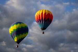 Six hot air balloons in various bright colors and patterns drifting through cloudy skies.
