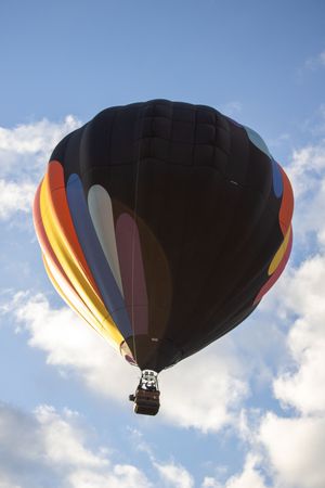 A black and orange hot air balloon floats against a blue sky with white clouds.