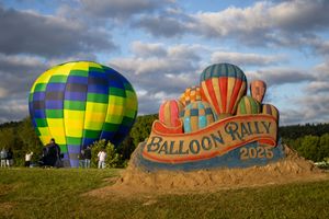 Large sand sculpture advertising Balloon Rally 2023 with hot air balloons in background.