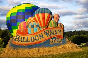 Sand sculpture for Balloon Rally event with colorful hot air balloons launching behind it.