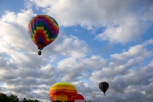 Multiple hot air balloons float in a bright blue sky with puffy white clouds.