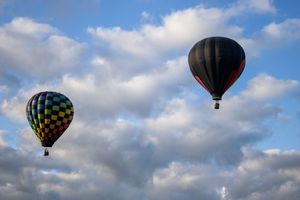 Black hot air balloons silhouetted against white clouds in blue sky.