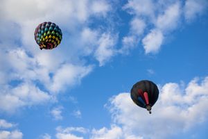Colorful hot air balloons float against a bright blue sky with white puffy clouds.