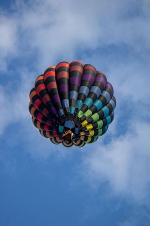 Vibrant rainbow-colored hot air balloon with circular pattern against blue sky.