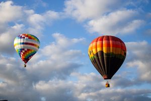Multiple hot air balloons soar through a cloudy blue sky during a balloon festival.