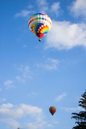 Hot air balloons of various colors and patterns drift through a clear summer sky.