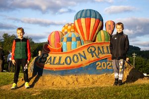 Balloon rally welcome sign on grassy hill with decorative elements.