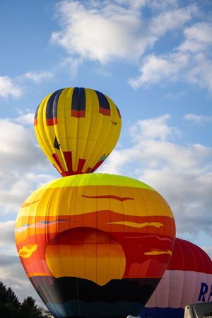 Yellow and red hot air balloons lined up against cloudy sky during festival.