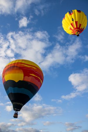 Hot air balloons with yellow and black designs float through blue skies with white clouds.