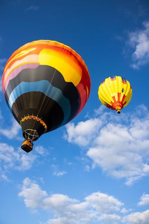 Colorful hot air balloons ascending in formation against bright blue sky with scattered clouds.
