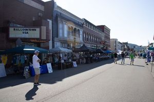 Street view of small town storefronts and sidewalks with vendor tents set up along the buildings.