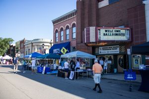 Row of brick buildings and storefronts along a small town main street with vendor tents.