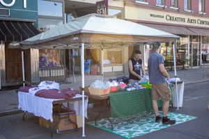 White vendor tents and displays line the sidewalk in front of brick commercial buildings.