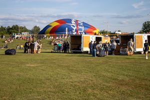 Outdoor festival setup with colorful tents and vendor booths spread across a grassy field on a sunny day.