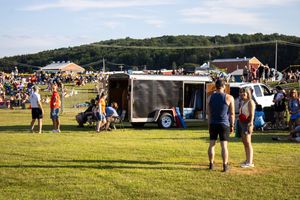 Festival attendees gathering near food trucks and vendor stalls on a grassy field.